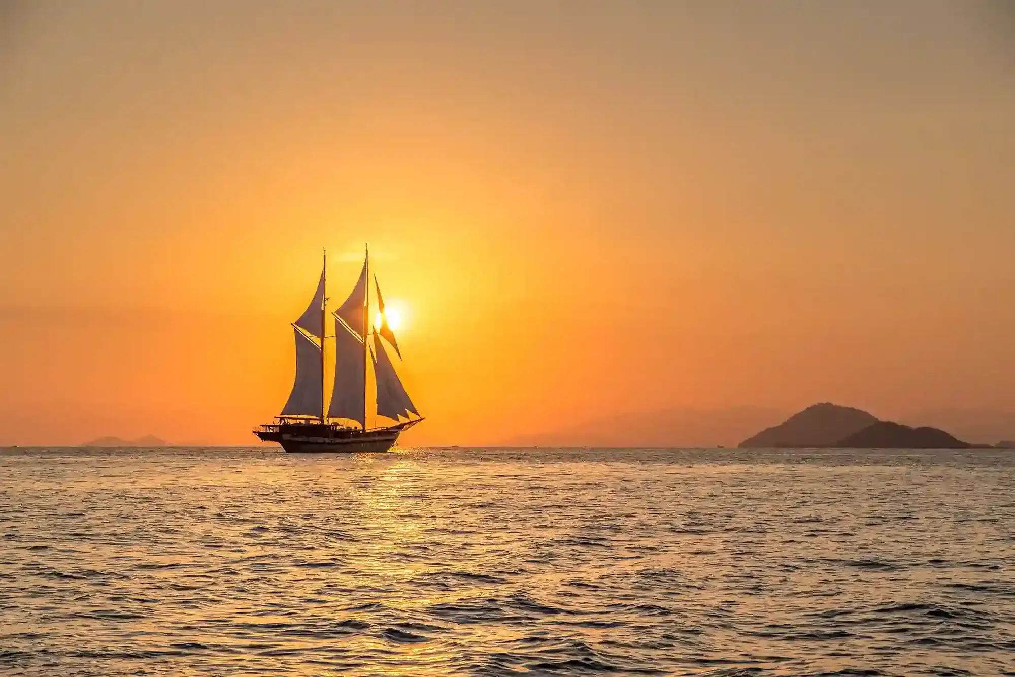 A white-sailed phinisi on open water at dusk