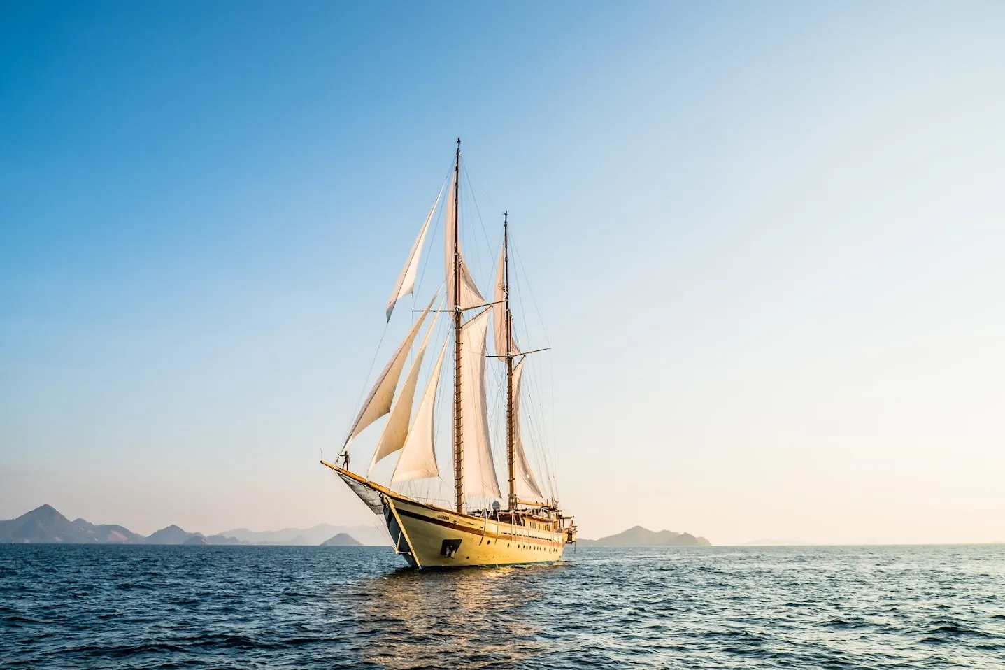 A phinisi under white sails in calm water