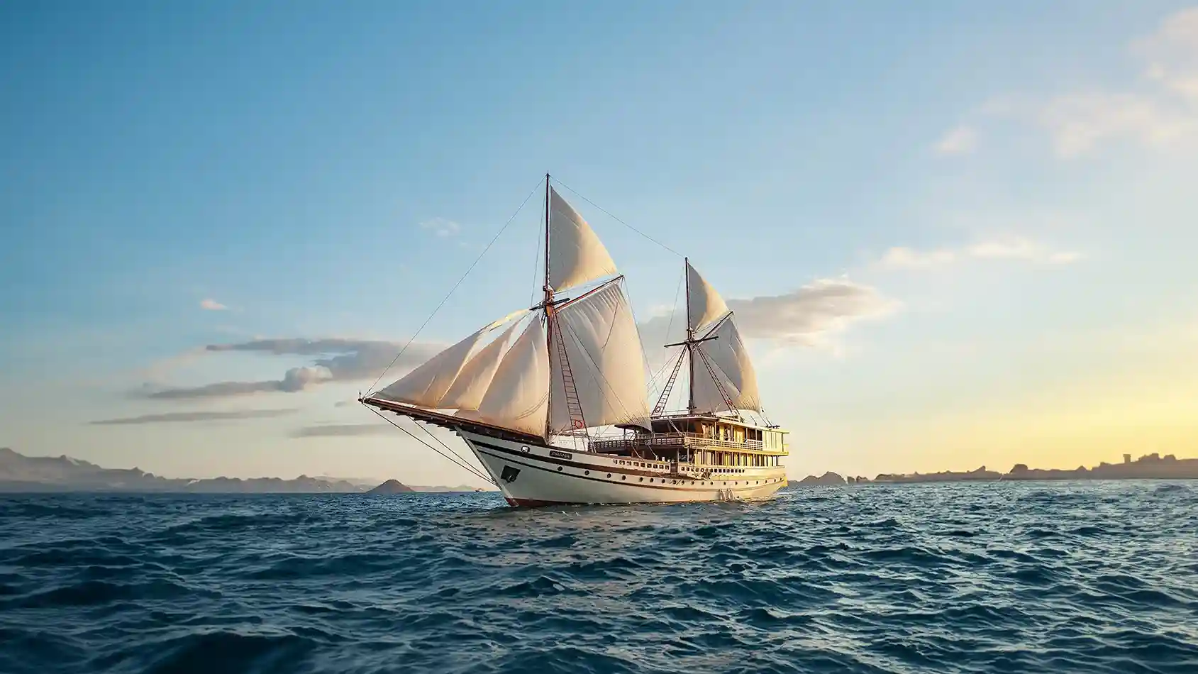 A large phinisi under sail against the Komodo hills