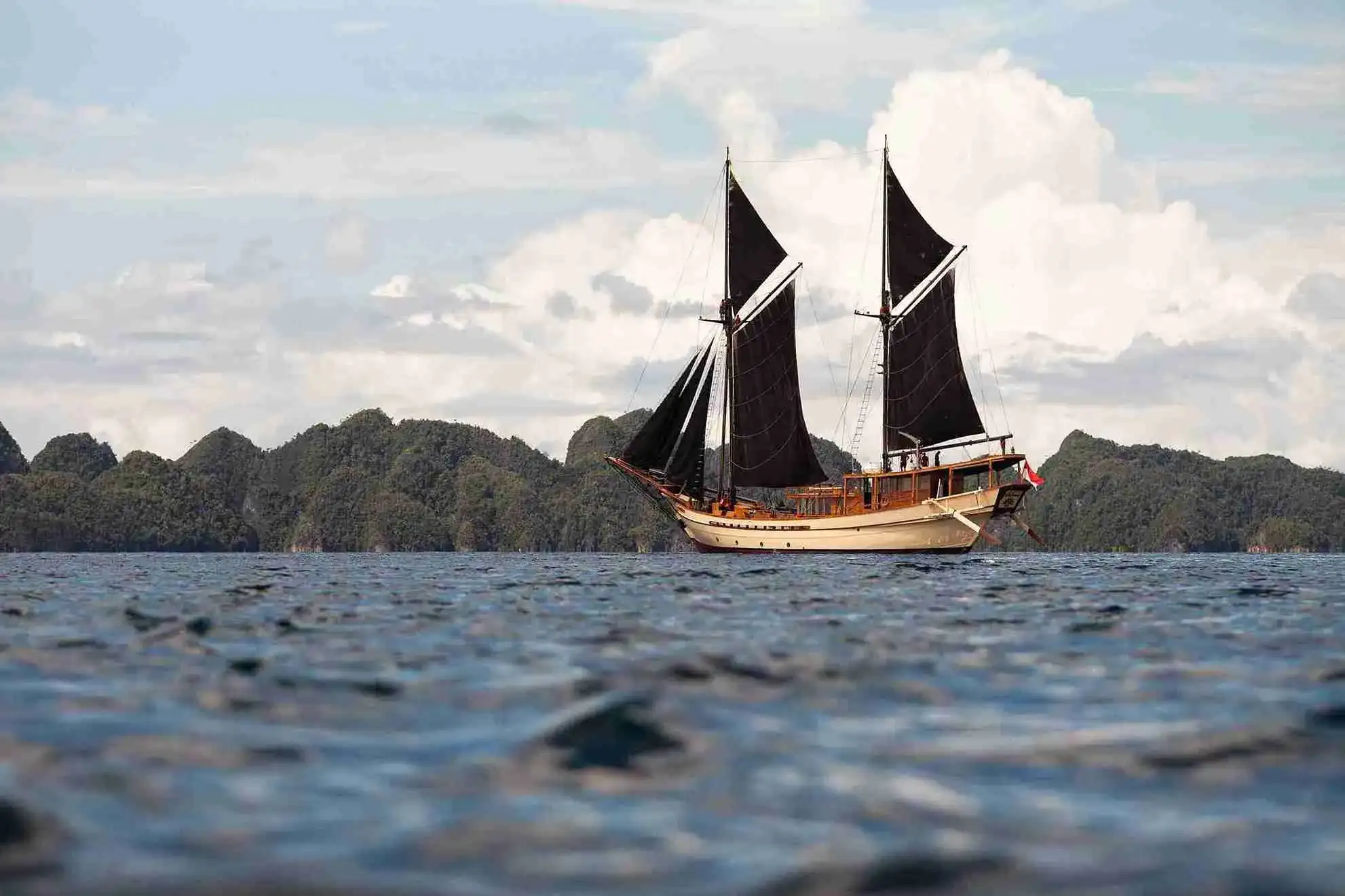 A dark-hulled phinisi under sail at dusk
